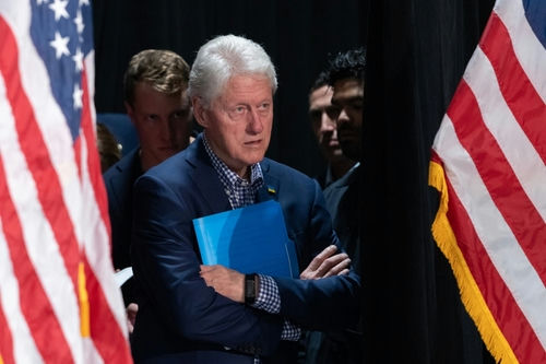 shutterstock2222838159-2jpg Bill Clinton standing between American flags with a folder.