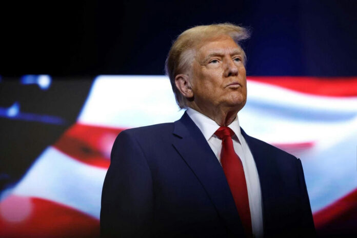 shutterstock2543144643 donald trump in suit with red tie American flag backdrop