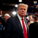 MAGA Base REVOLTS: Trump Posted WHAT?! A serious-looking man in a suit with a red tie surrounded by a crowd and cameras