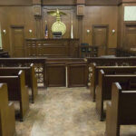 Billionaire Funding BOMBSHELL: Carroll Under DOJ Lens Empty courtroom with wooden benches and judges bench.