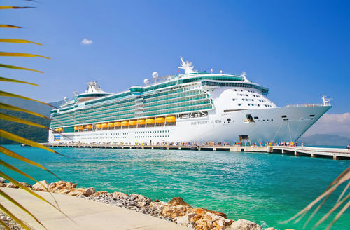 shutterstock_536760823 Large cruise ship docked near turquoise water and foliage.