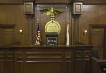 Accused Heir Demands Parents’ Cash Judges bench in an empty courtroom, scales emblem above.