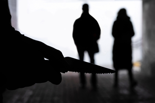 Silhouette,Of,A,Man,With,A,Knife,On,The,Background Silhouette of a person holding a knife with two figures in the background