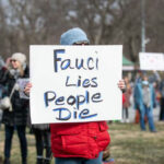 Person holding sign that reads Fauci Lies People Die