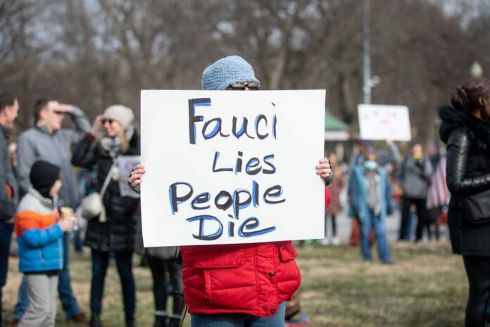 shutterstock_2115278627-1 Person holding sign that reads Fauci Lies People Die