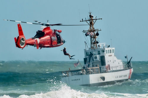shutterstock_2307202521-1 Coast Guard training with helicopter and boat in rough seas.