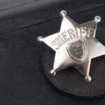 Trump Immunity Plea Amid Sheriff Death Threats Sheriff badge on black leather surface.