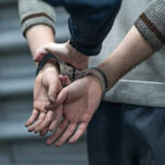Blindfolded Man Sparks Global Mystery Person in handcuffs being detained by another person.