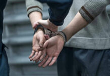 Blindfolded Man Sparks Global Mystery Person in handcuffs being detained by another person.