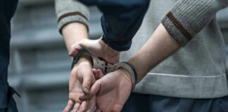 Person in handcuffs being detained by another person.