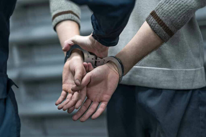1904367880 Person in handcuffs being detained by another person.