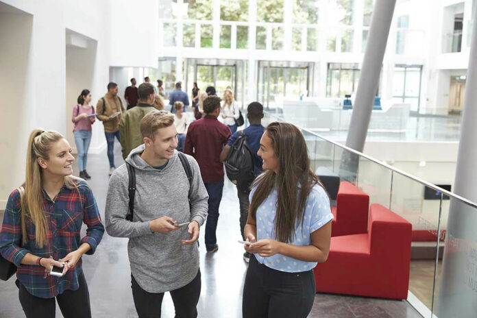 478513864 Students conversing in bright school hallway.