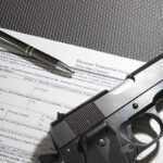 Supreme Stall Supercharges Gun Rights Chaos Form with gun and pen on table.