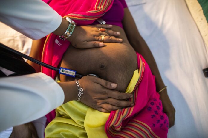 Maternal-Mortality40-1602x1068-2 A healthcare professional examining a pregnant woman's abdomen with a stethoscope