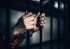 Illegal Trucker, Triple Deaths—Light Sentence? Hands gripping prison bars, suggesting confinement
