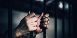 Hands gripping prison bars, suggesting confinement