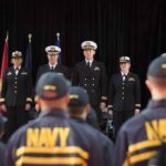Navy officers stand at attention on stage during a ceremony