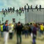 Crowd and people climbing large border wall during protest.