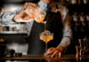 Bartender pouring a cocktail into a glass.