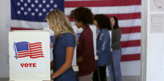 People voting in booths with U.S. flags in background.