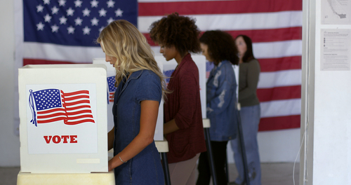 People voting in booths with U.S. flags in background.