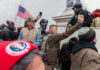 People at U.S. Capitol riot, holding flags and phones.