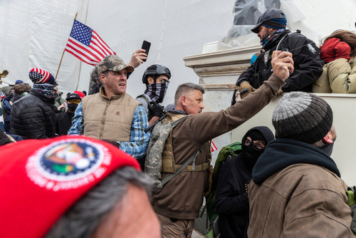 People at U.S. Capitol riot, holding flags and phones.