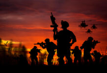 Silhouetted soldiers and helicopters against a sunset sky.